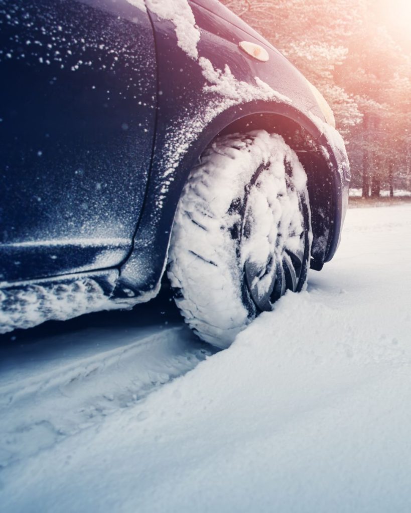 Close-up of a car tire driving through deep snow on a winter road.